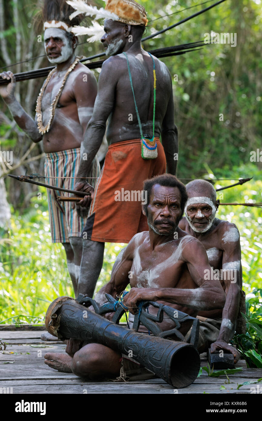 Headhunter of a tribe of Asmat in traditional dresses and painting with drum. Stock Photo