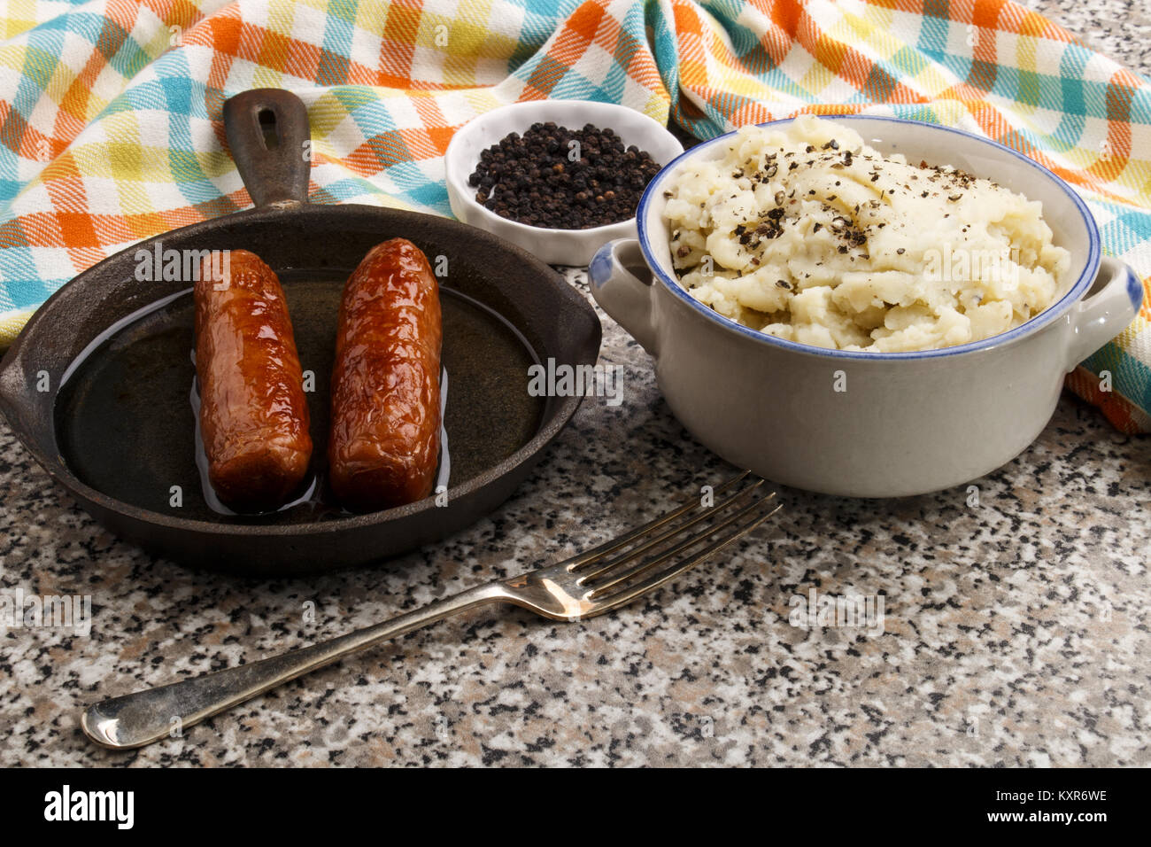 peppered mashed potato in a bowl and grilled british sausages in a small cast iron pan Stock