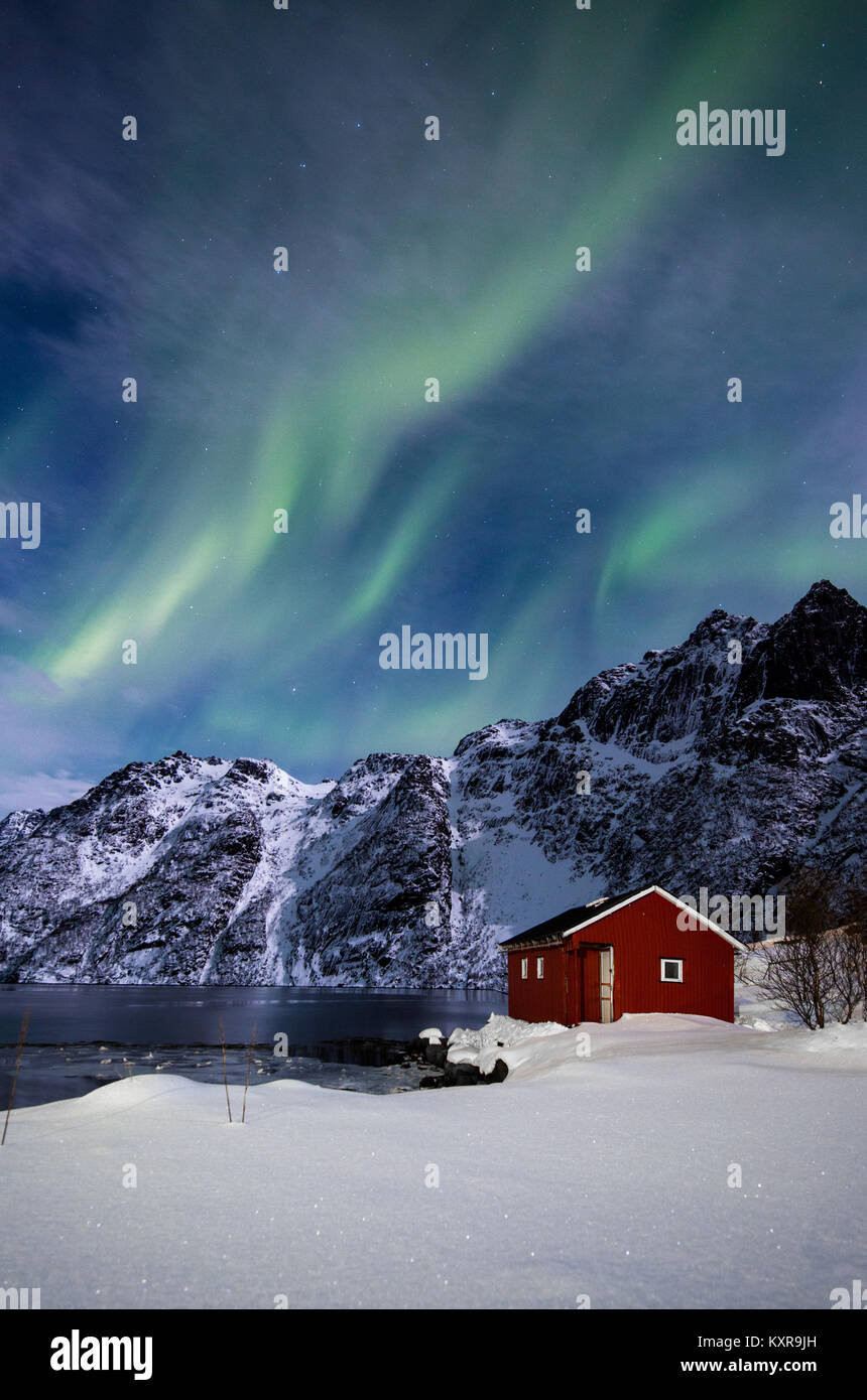 Lofoten, Svolvaer, Aurora Borealis over a frozen lake and red rorbu, Norway. Stock Photo