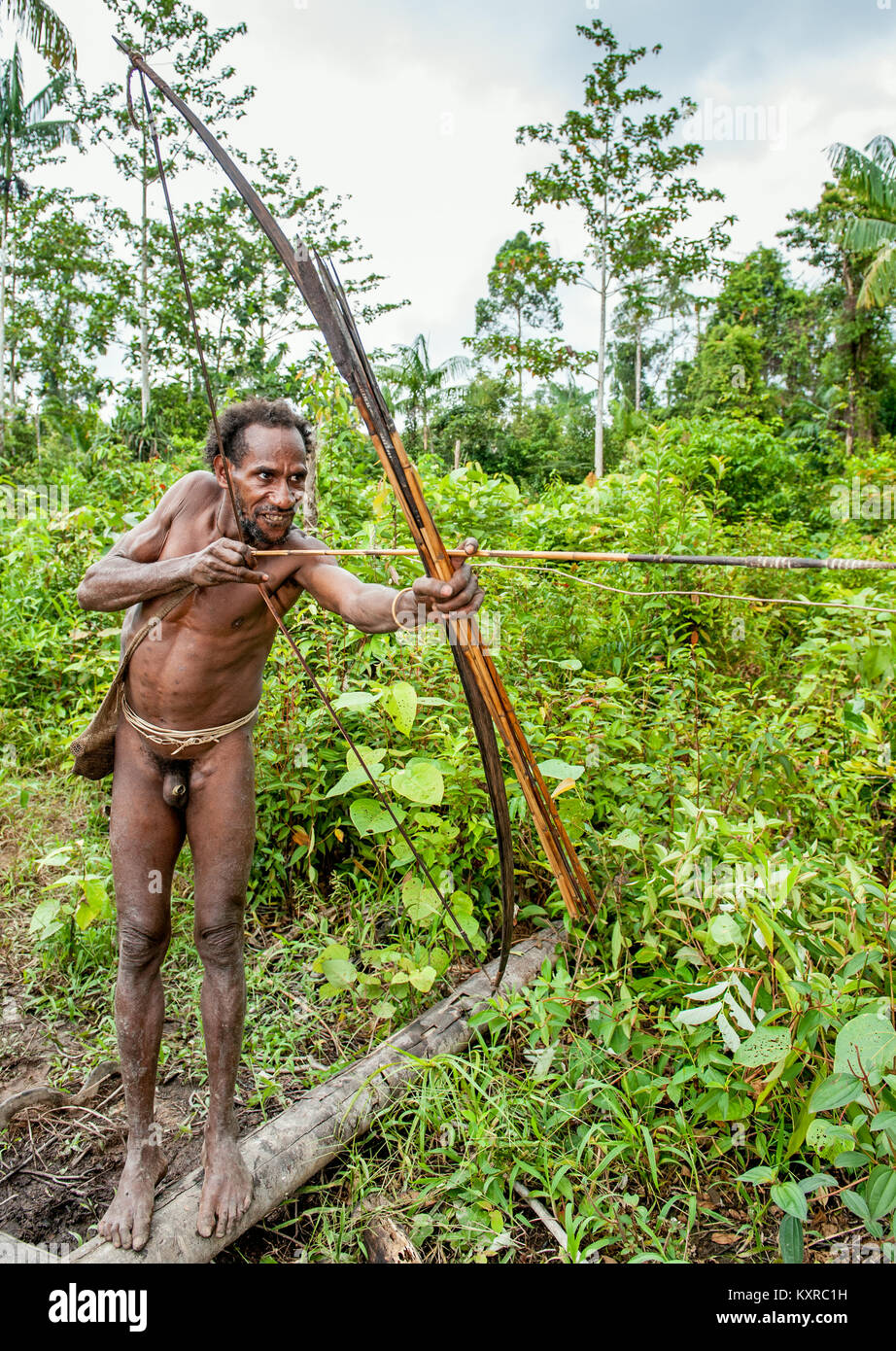 Korowai tribe. Papuan shooting arrows from a bow. Natural green jungle background. Stock Photo