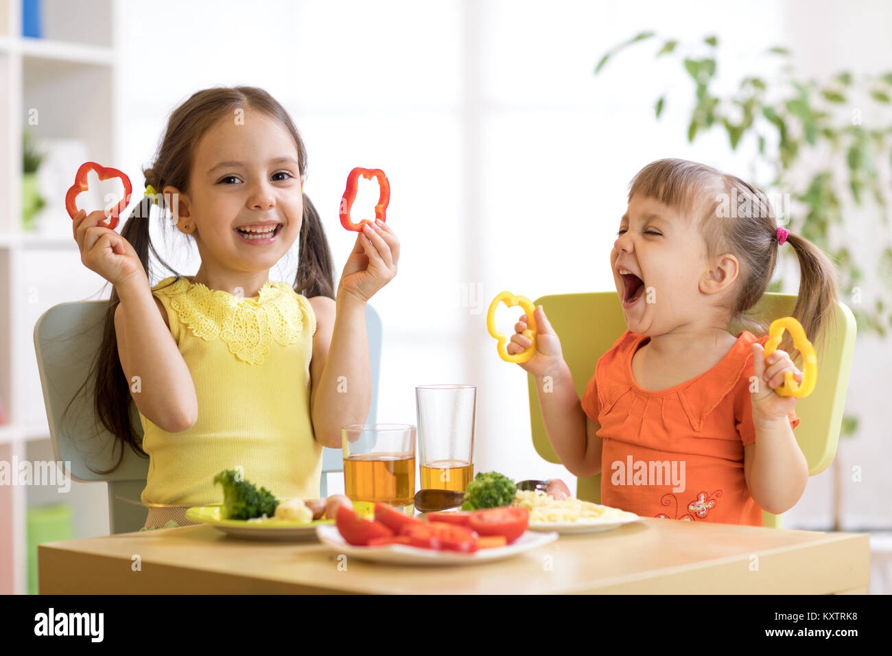 Funny playful children girls eating healthy food. Kids lunch at home or kindergarten. Stock Photo