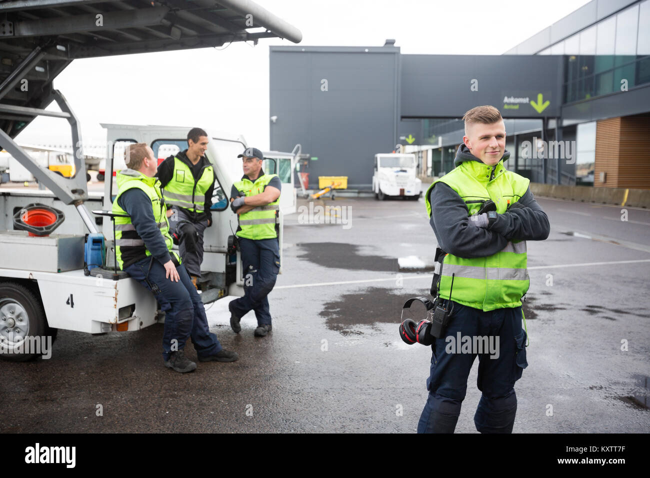 Confident male worker standing arms crossed while colleagues communicating at gangway on runway Stock Photo