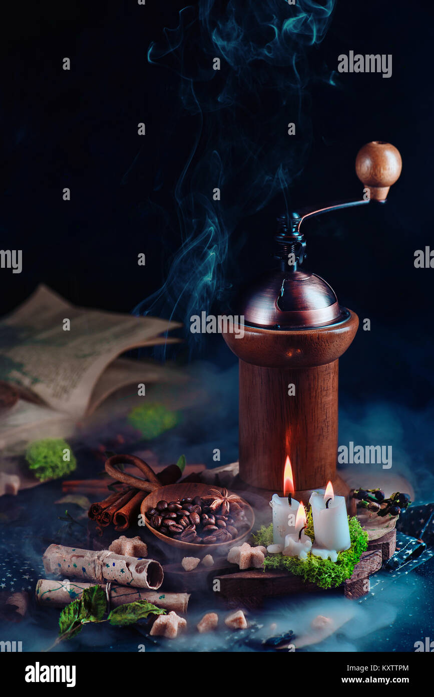 Vintage coffee grinder with coffee beans, star0shaped sugar, and burning candles. Magical still life with open book and copy space. Alternative coffee Stock Photo