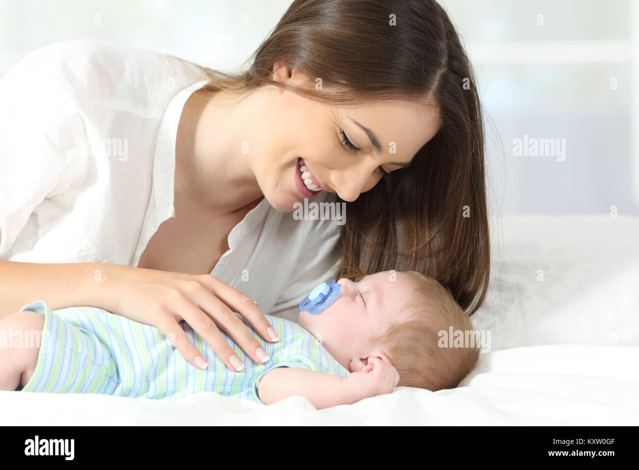 Portrait of a proud mother enjoying with her baby sleeping on a bed Stock Photo