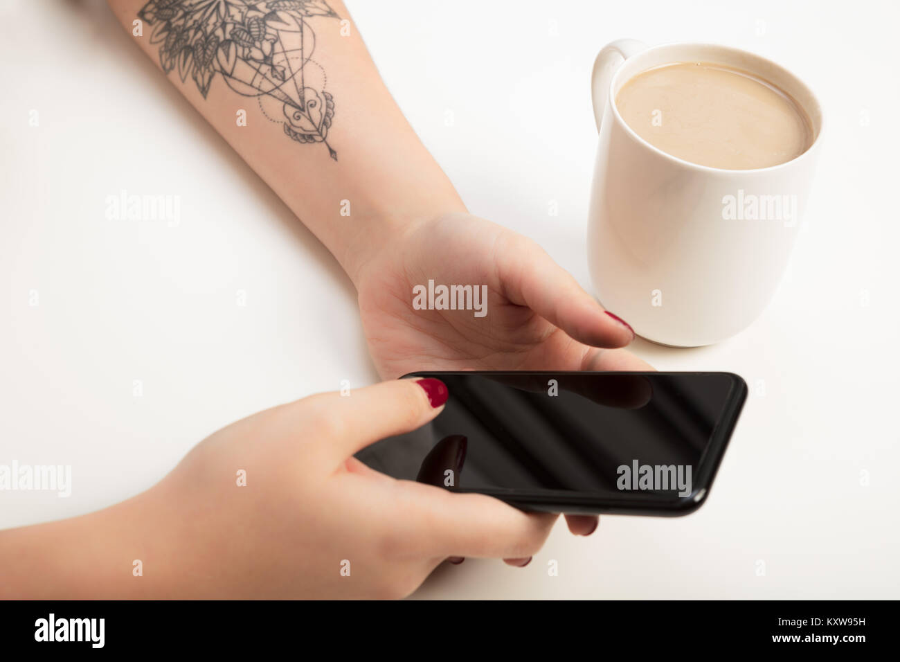 Woman banking , shopping or booking on a mobile phone in a close up view of her hands and the blank screen alongside a mug of coffee or tea Stock Photo