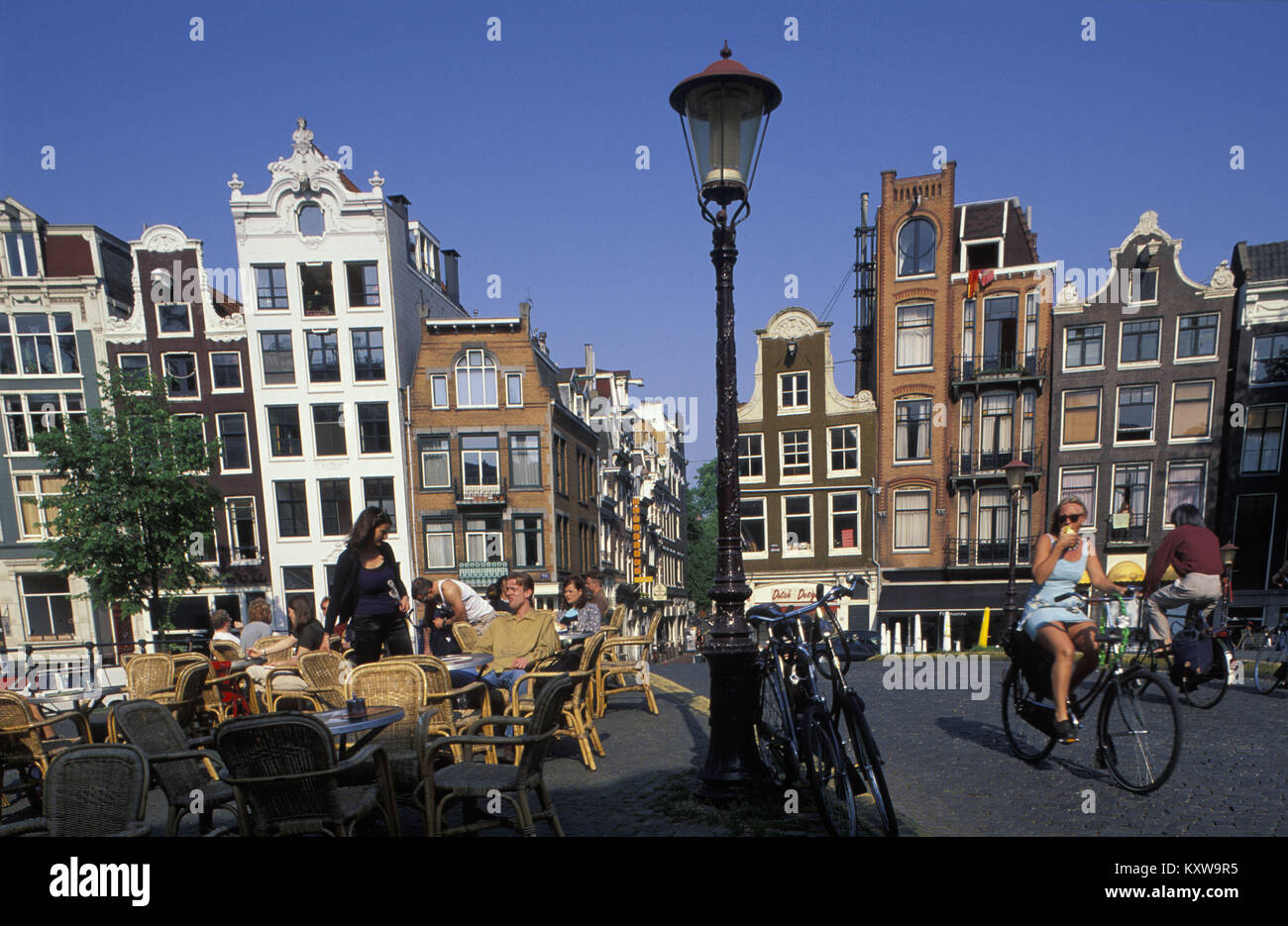 The Netherlands, Amsterdam, Canal called Singel. UNESCO World heritage Site. People sitting on terrace of outdoor cafe. Cyclists. 17th century. Stock Photo