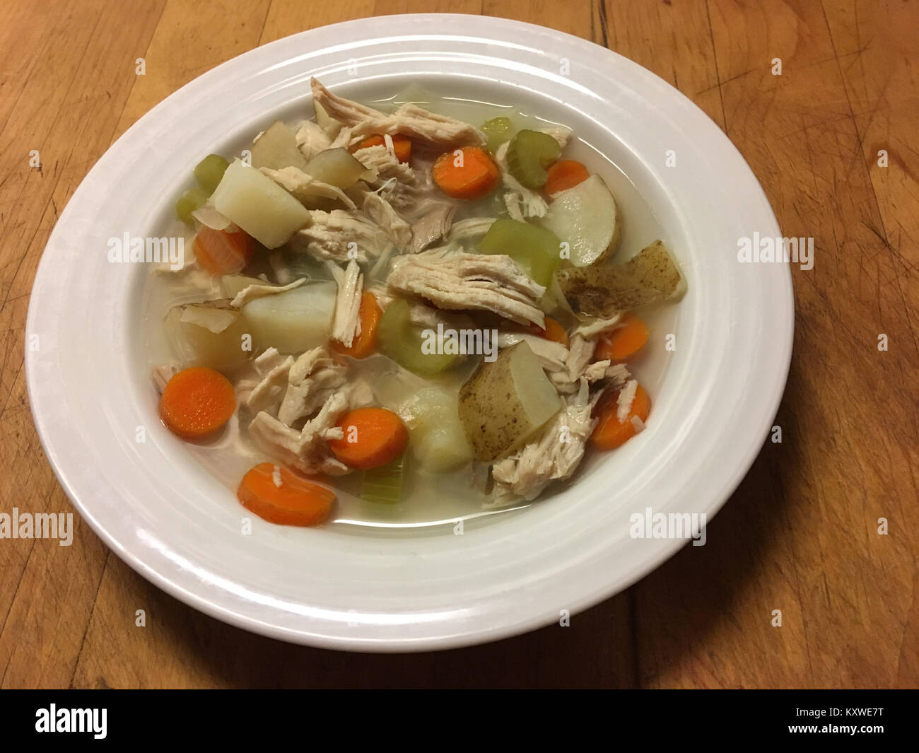 Bowl of homemade chicken vegetable soup on wooden cutting board Stock Photo