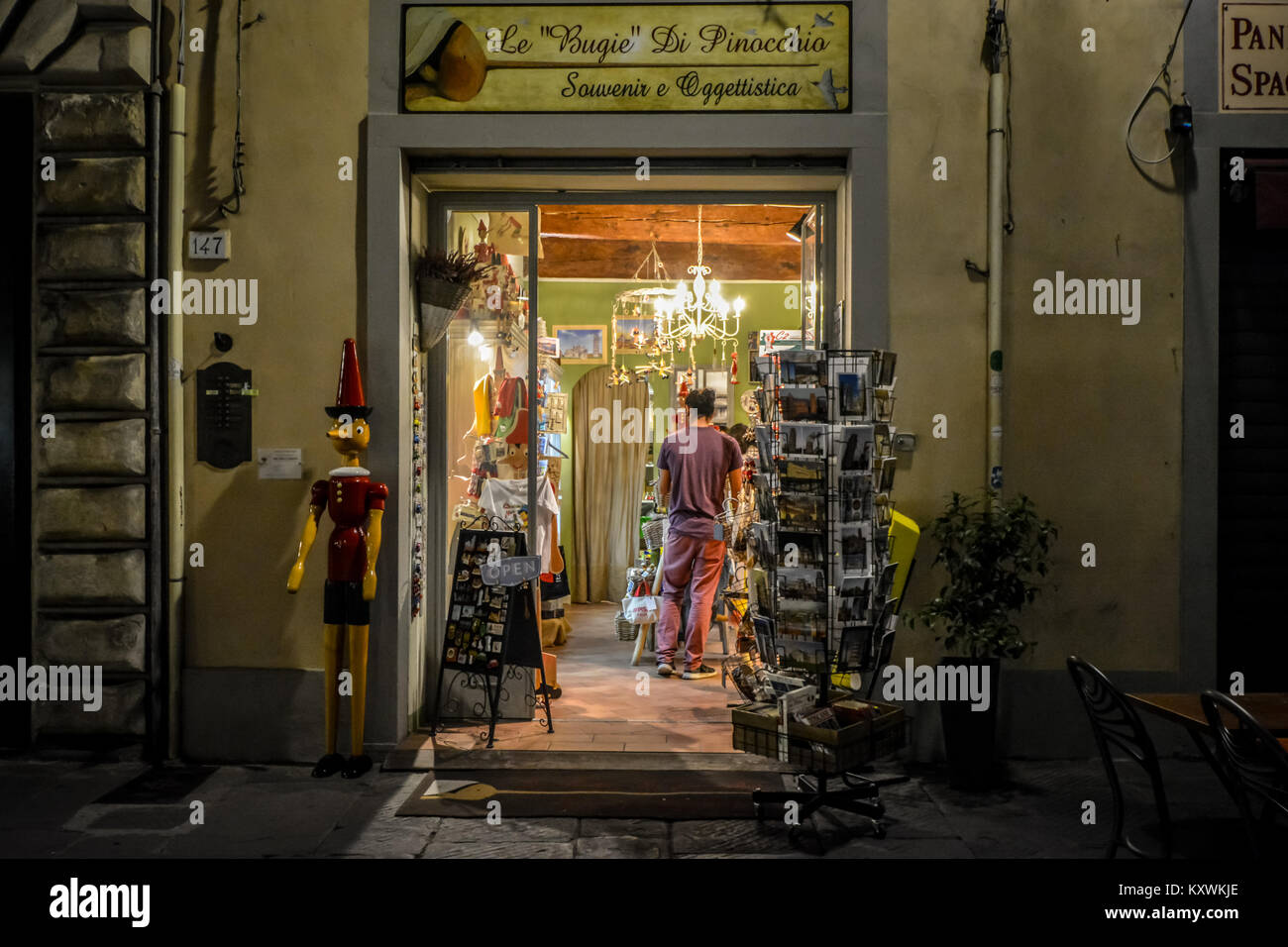 An oversize Pinocchio marionette puppet outside a gift and souvenir shop in Pisa Italy late in the evening with a customer inside Stock Photo