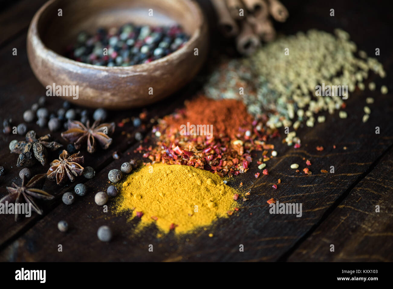 different kinds of pepper in bowl and spices with herbs scattered on wooden tabletop Stock Photo