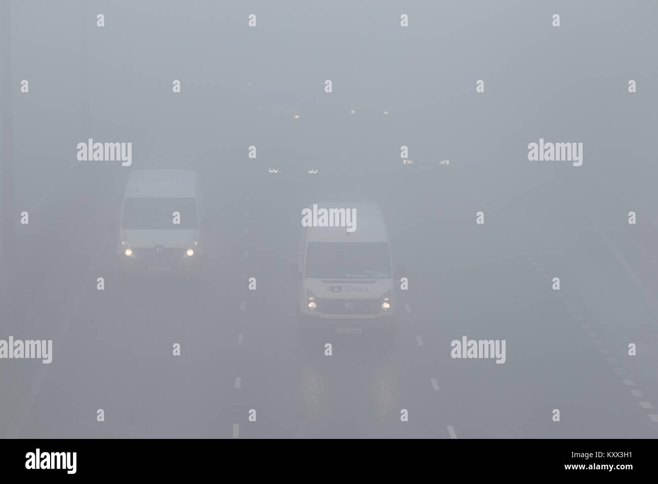 cars and vans driving on motorway without foglights on a foggy day in