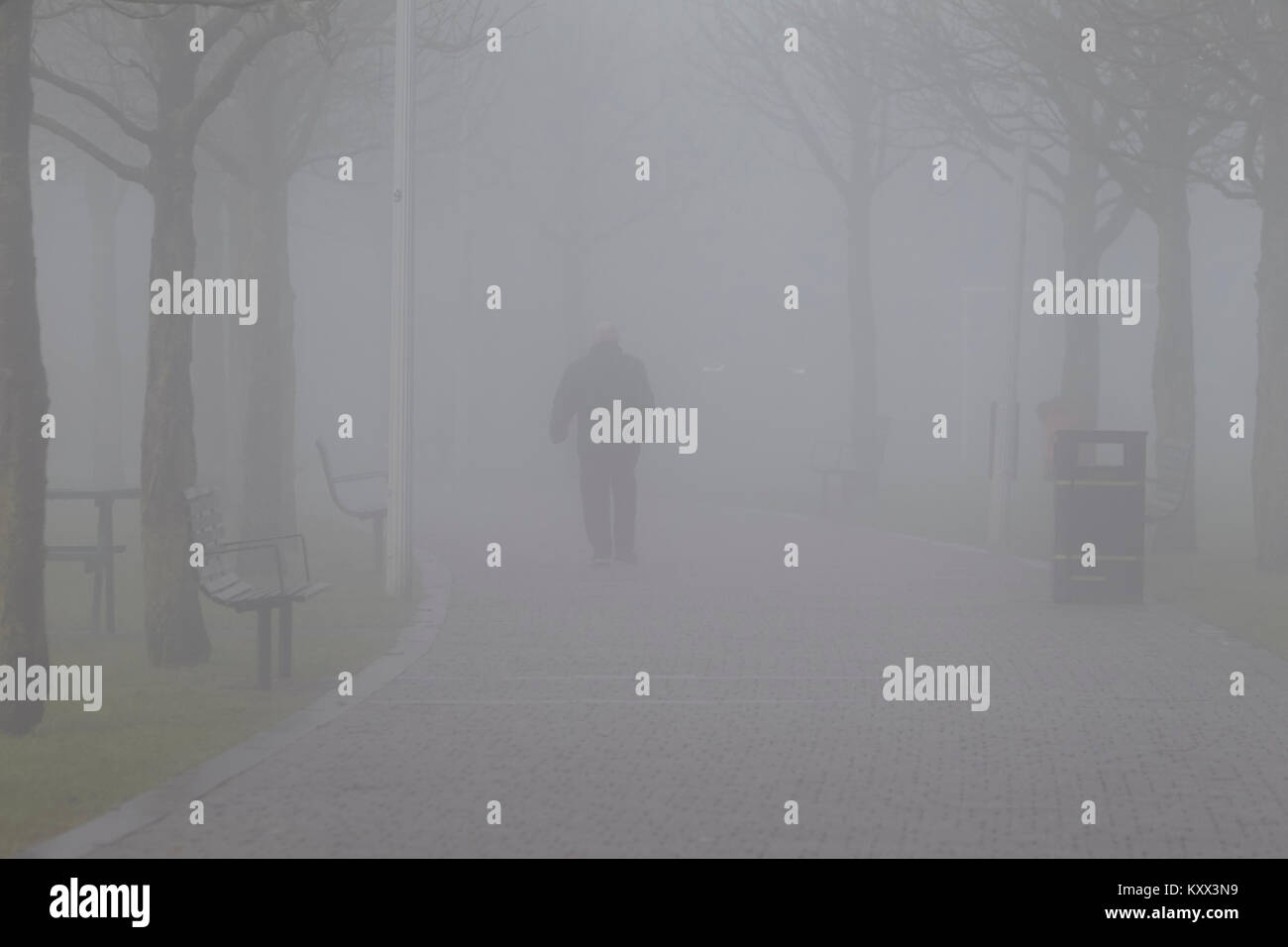 man walking along path towards car headlights on foggy day in the uk Stock Photo