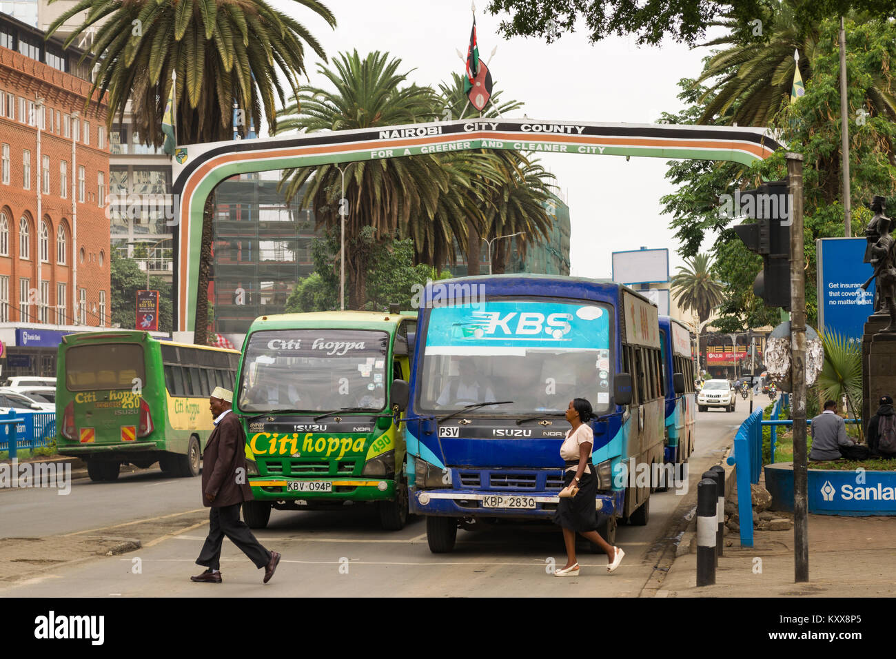 View down Kenyatta Avenue with the Nairobi City County sign above the road as buses wait at the traffic lights and pedestrians cross the road, Nairobi Stock Photo