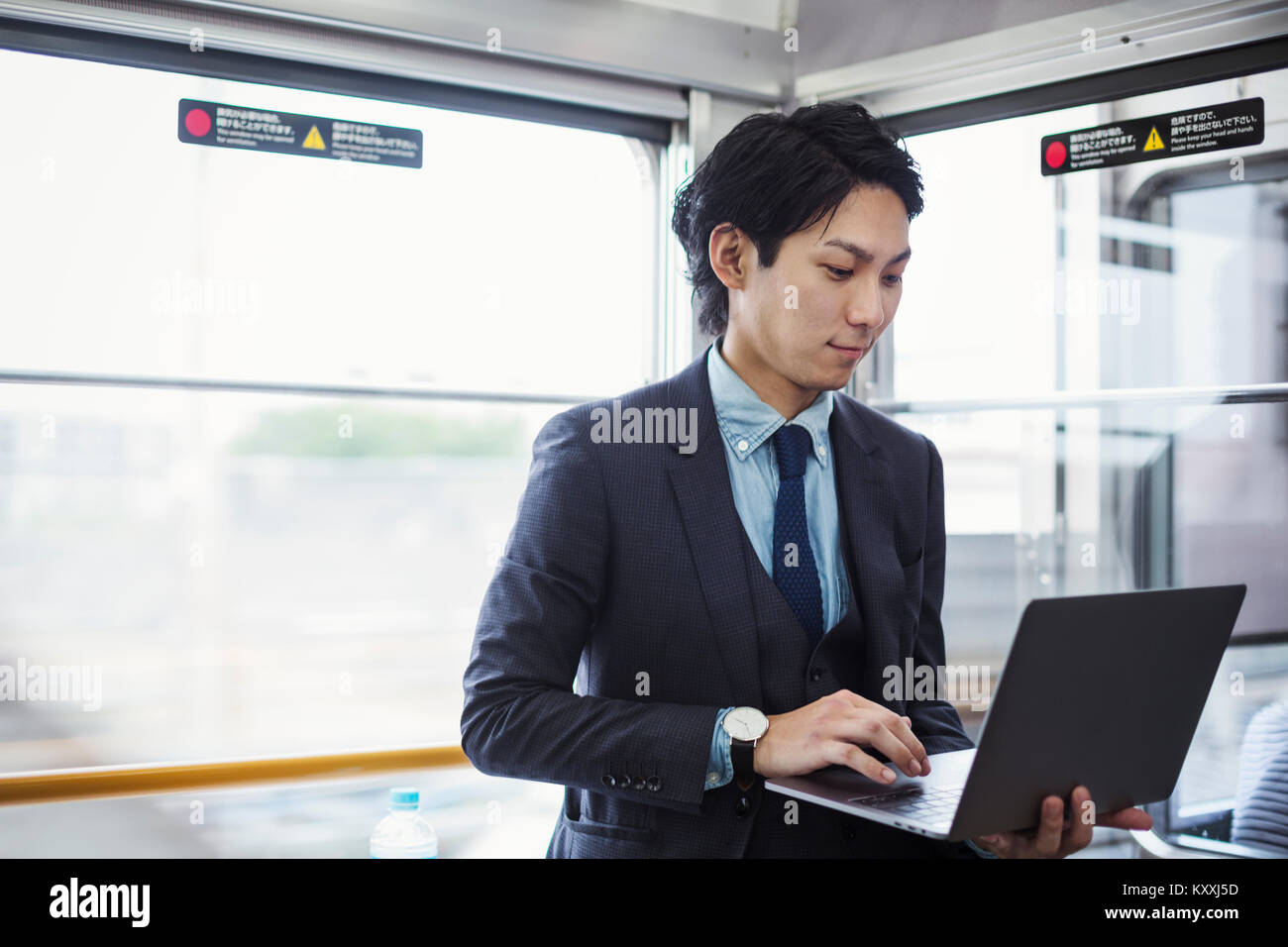 Businessman wearing suit standing on a commuter train, holding laptop