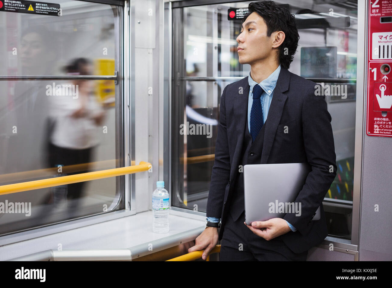 Businessman wearing suit standing on a commuter train, holding laptop