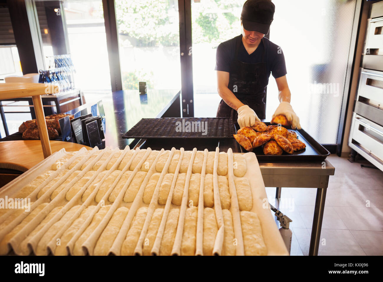 Man working in a bakery, wearing oven gloves, placing freshly baked