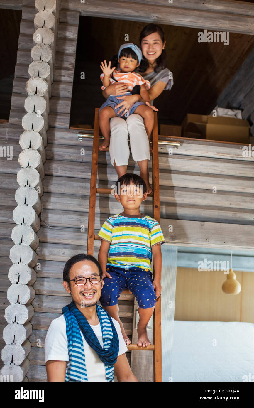 Family, man, woman, boy and young girl sitting on a ladder, smiling at camera. Stock Photo