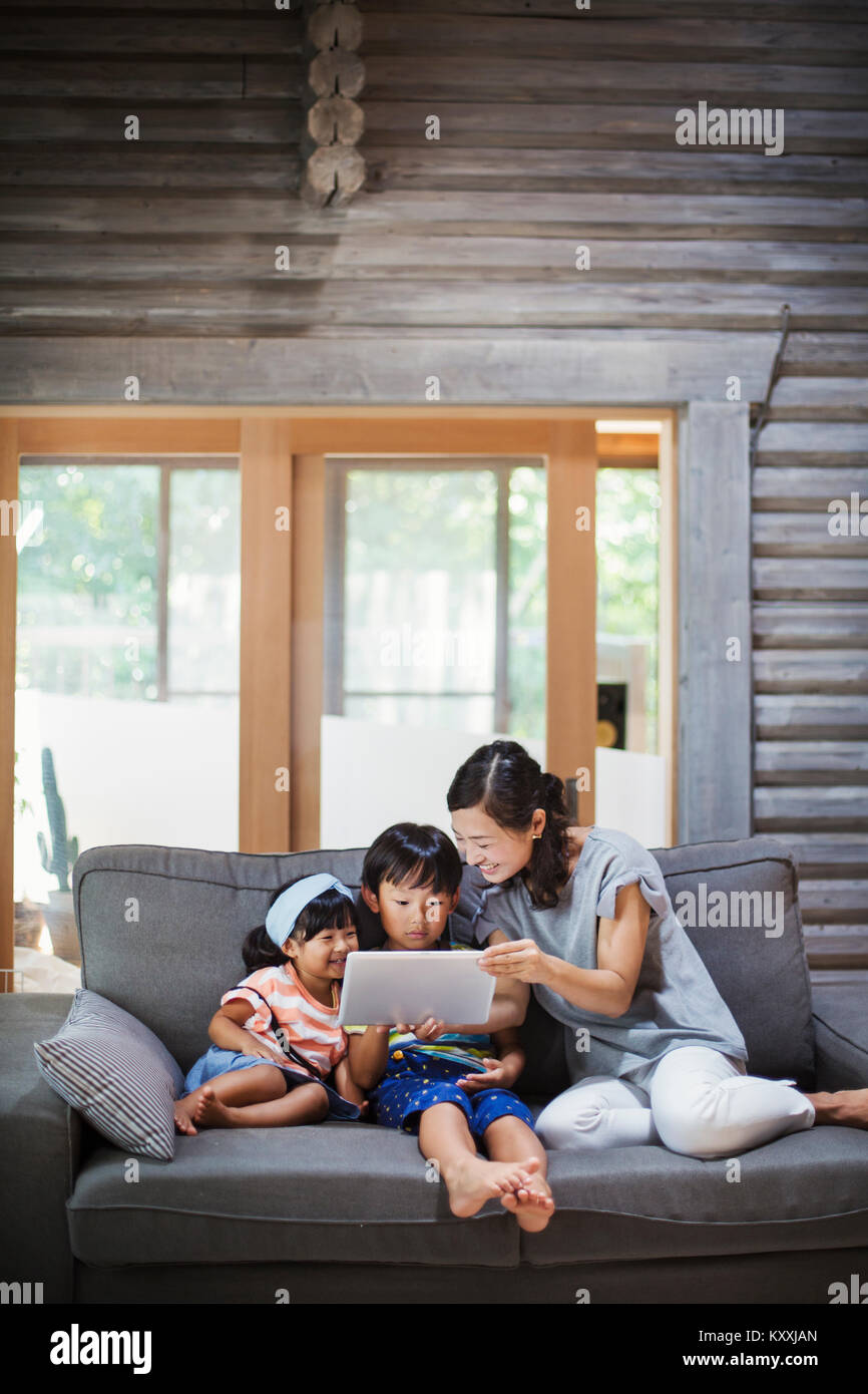 Woman, boy and young girl sitting on a grey sofa, looking at digital tablet. Stock Photo