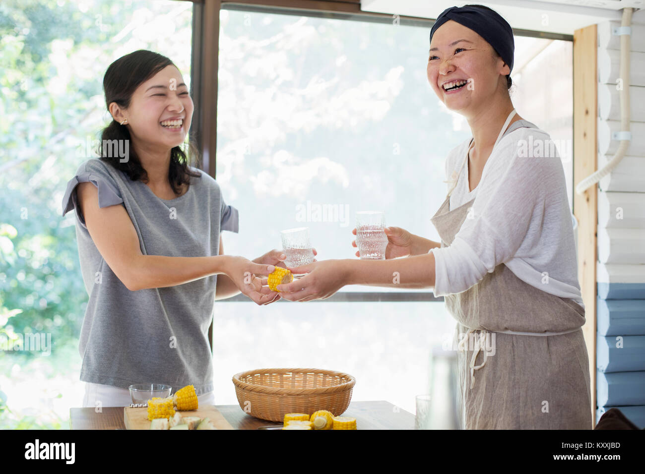 Two smiling women standing indoors at a table, holding drinking glasses. Stock Photo