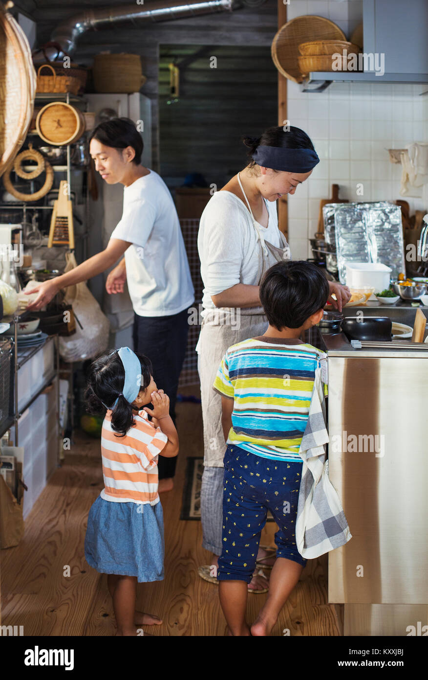 Man, woman wearing apron, boy and young girl standing in a kitchen, preparing food. Stock Photo