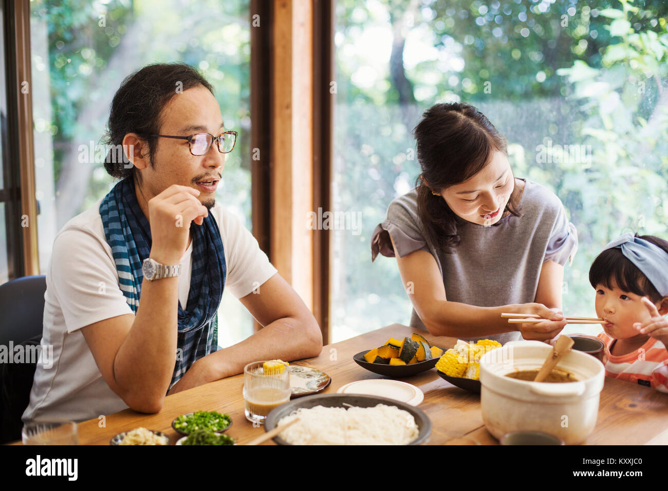 Man, woman and young girl sitting round a table with bowls of food, eating together. Stock Photo