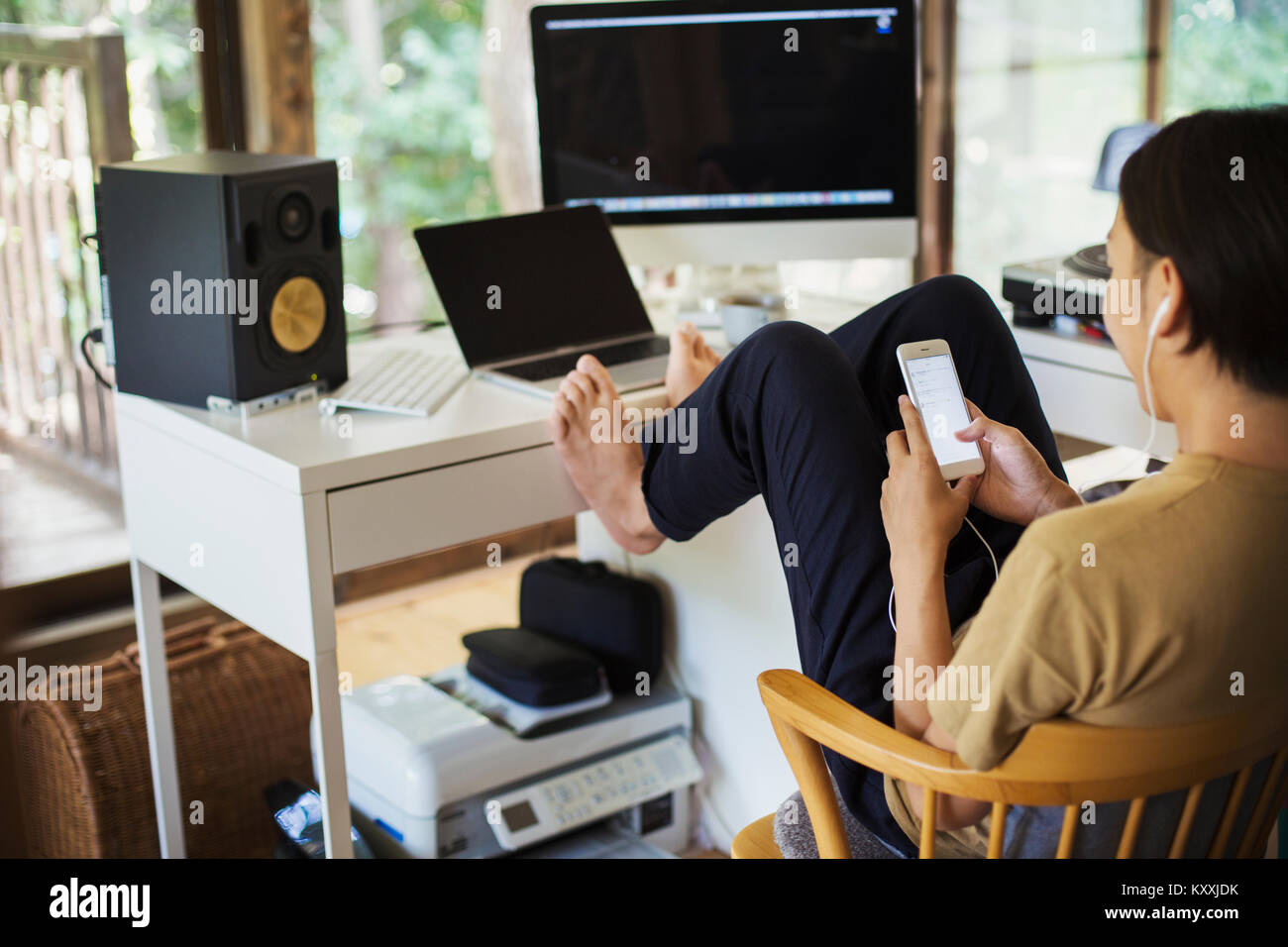 Man sitting indoors at a desk with computer, legs raised, barefoot