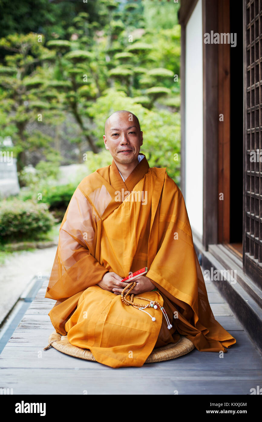 Buddhist monk with shaved head wearing golden robe sitting on floor