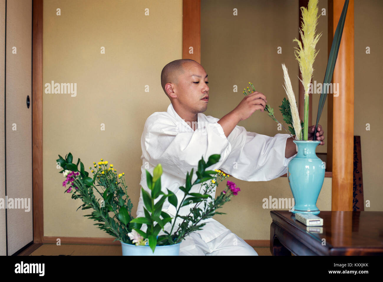 Buddhist monk with shaved head wearing white robe kneeling on floor
