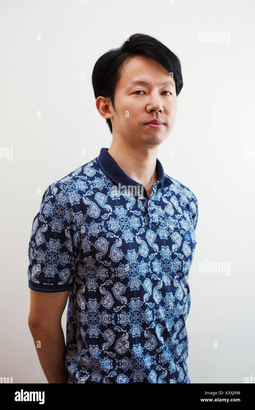 Portrait of man with short black hair wearing blue patterned shirt standing in art gallery, looking at camera. Stock Photo