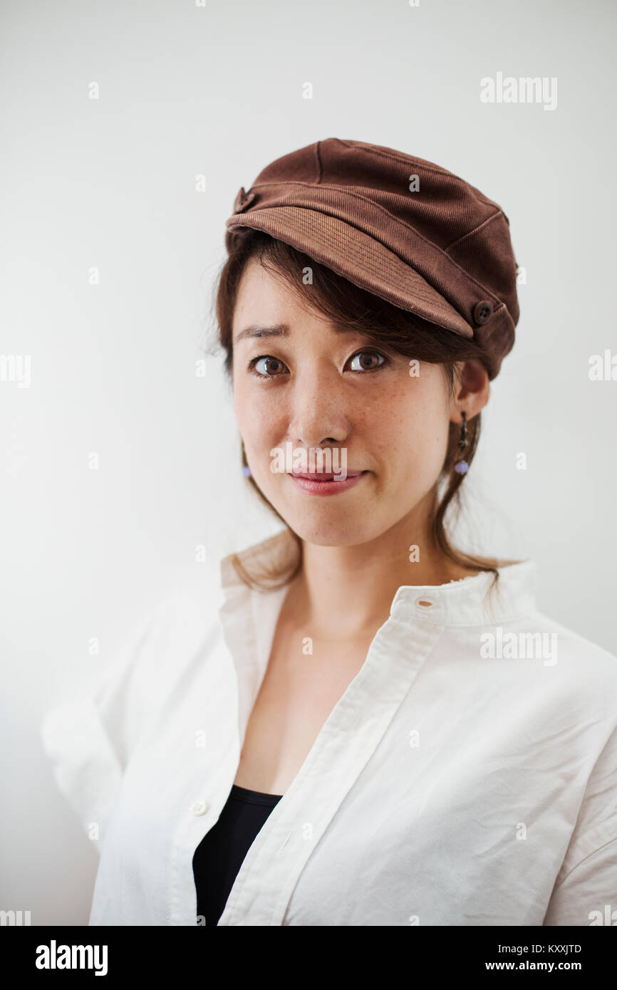 Woman wearing white shirt and brown cap standing in art gallery, smiling at camera. Stock Photo
