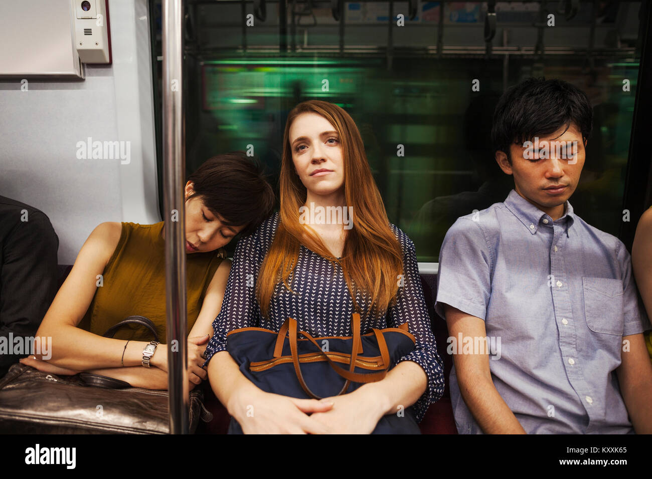 Three people, two women and man, sitting side by side on a subway train, Tokyo commuters. Stock Photo