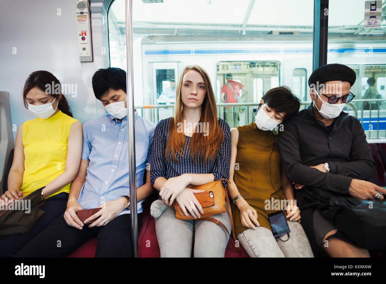 Five people wearing dust masks sitting sidy by side on a subway train, Tokyo commuters Stock
