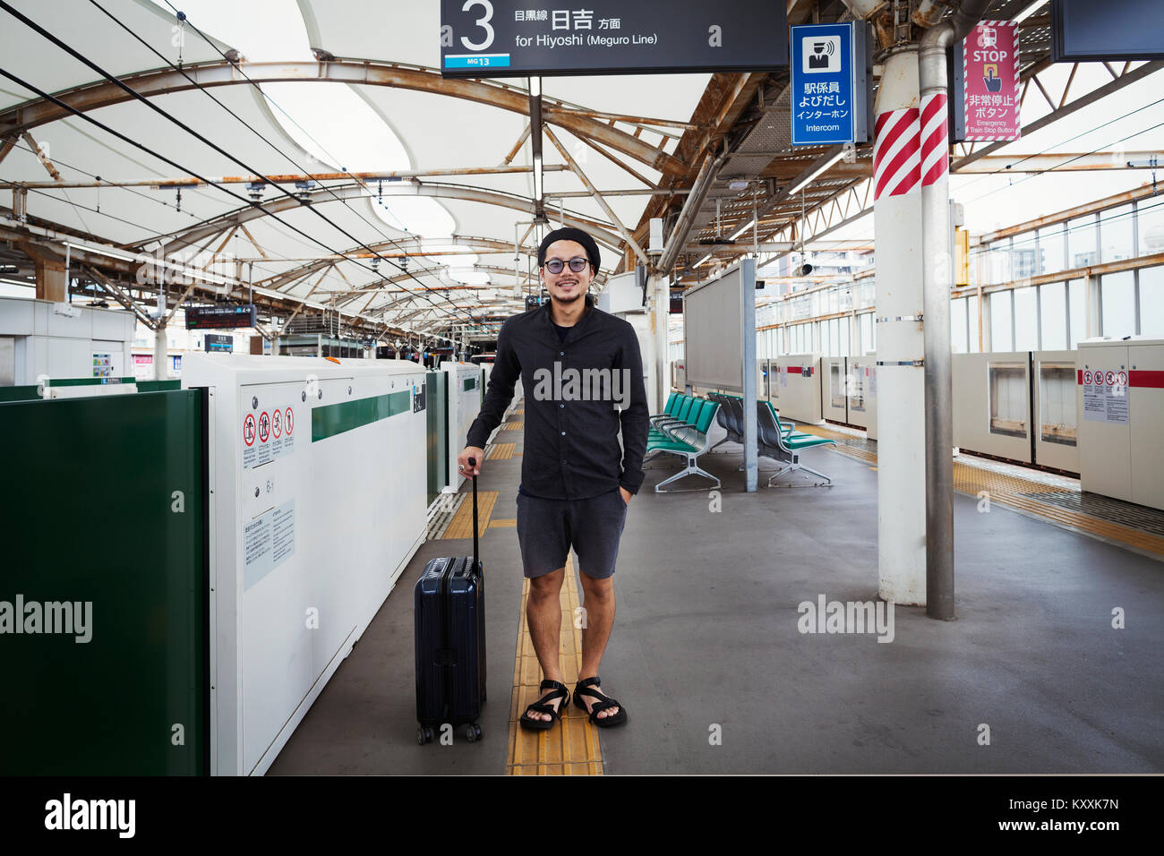 Smiling man with wheeled suitcase standing on the platform of a subway station, Tokyo commuter. Stock Photo