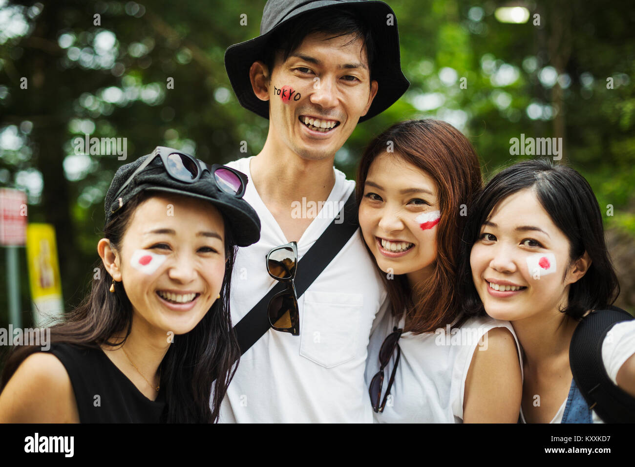 Smiling man and three young women standing outdoors, faces painted with  Japanese flags, looking at camera. Stock Photo