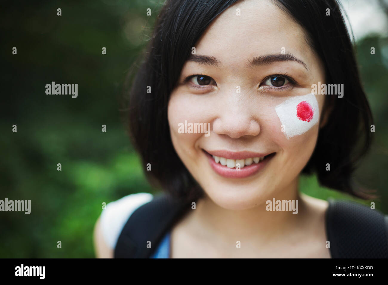 Portrait of young woman with black hair, Japanese flag painted on her cheek...