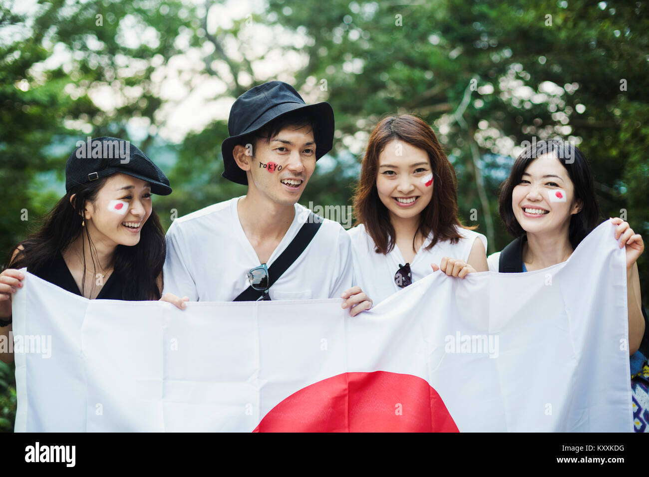 Smiling man and three young women standing outdoors, faces painted, holding Japanese flag. Stock Photo