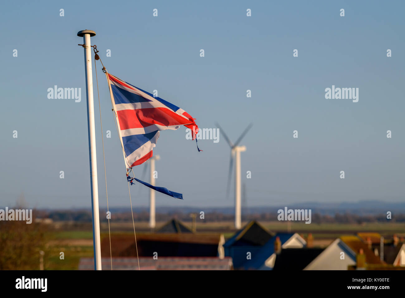 A tattered Union Jack flag fluttering in the wind against a blue sky. Stock Photo
