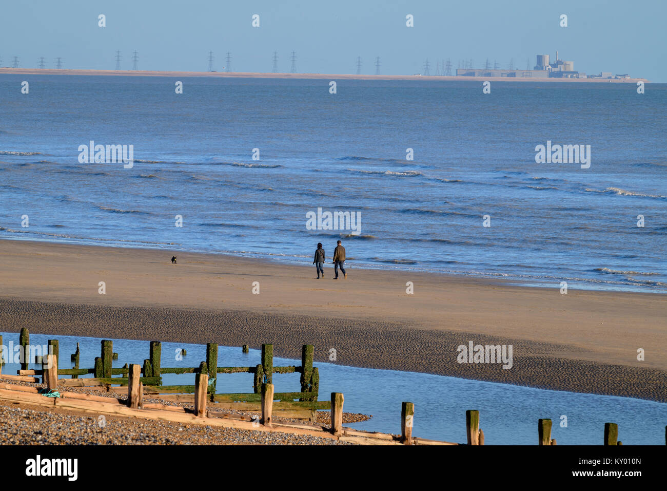 Dungeness power station in the distance as a couple stroll on WInchelsea Beach. Stock Photo