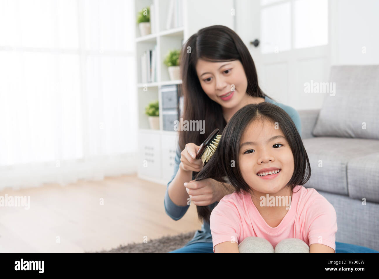 smiling pretty mother using brush helping happy cute little daughter combing hair. Stock Photo