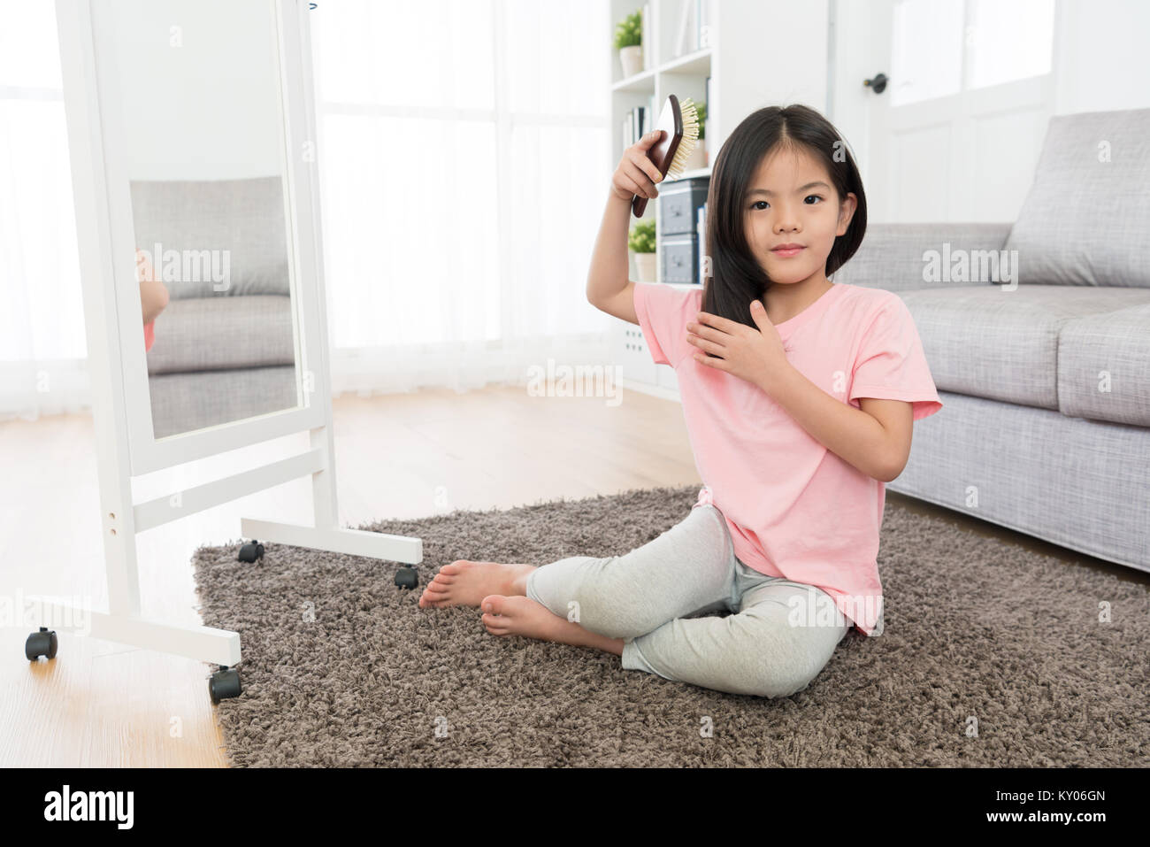 cute pretty little girl sitting on living room floor looking at camera and using brush combing hair in morning when she wake up. Stock Photo