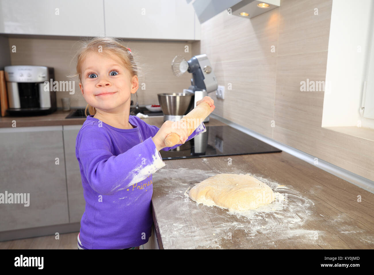 Girl using rolling pin for dough. Little girl baking. Сhild learns to cook Stock Photo