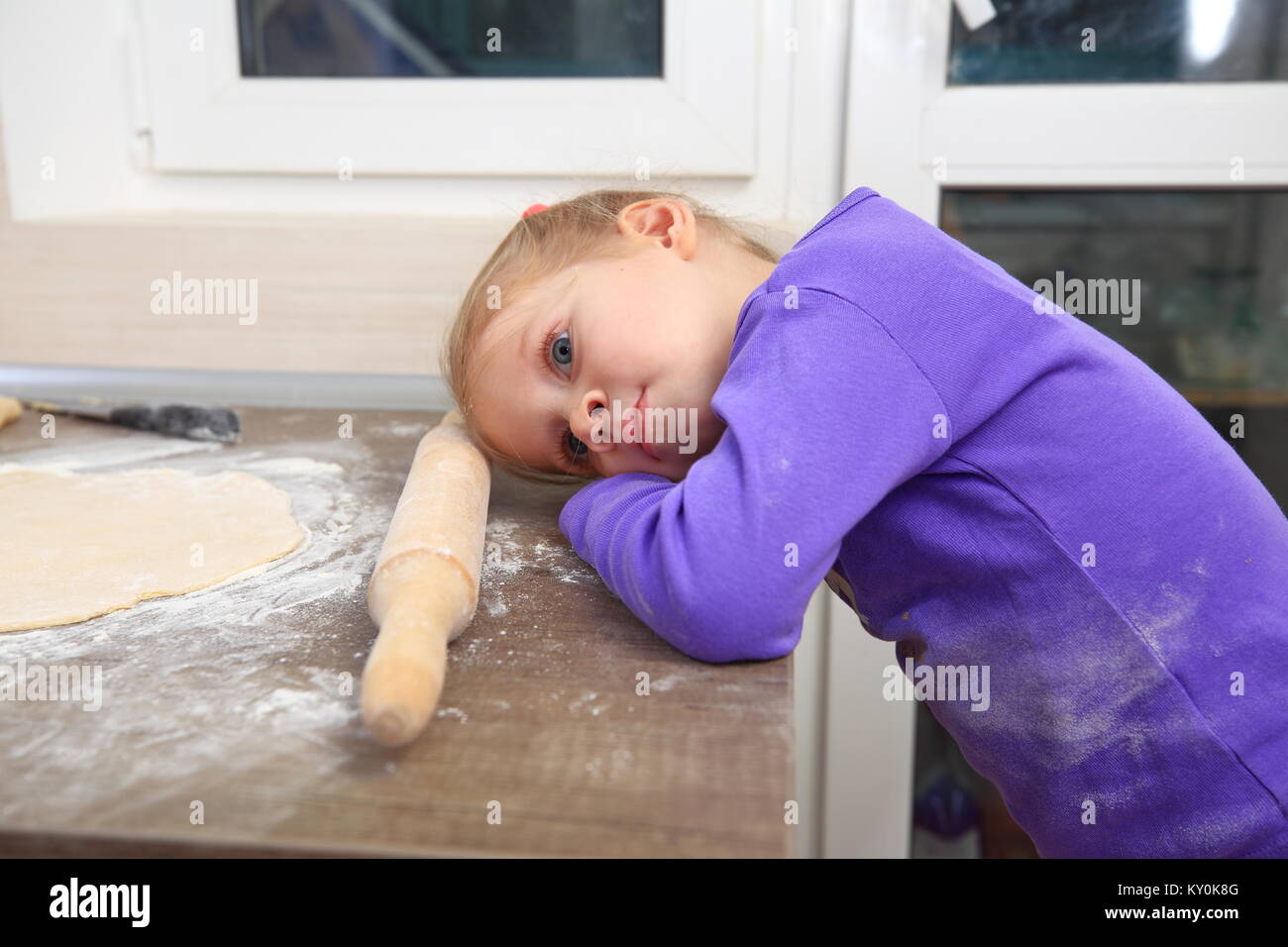 Tired little girl in the kitchen. Child tired to cook. Stock Photo