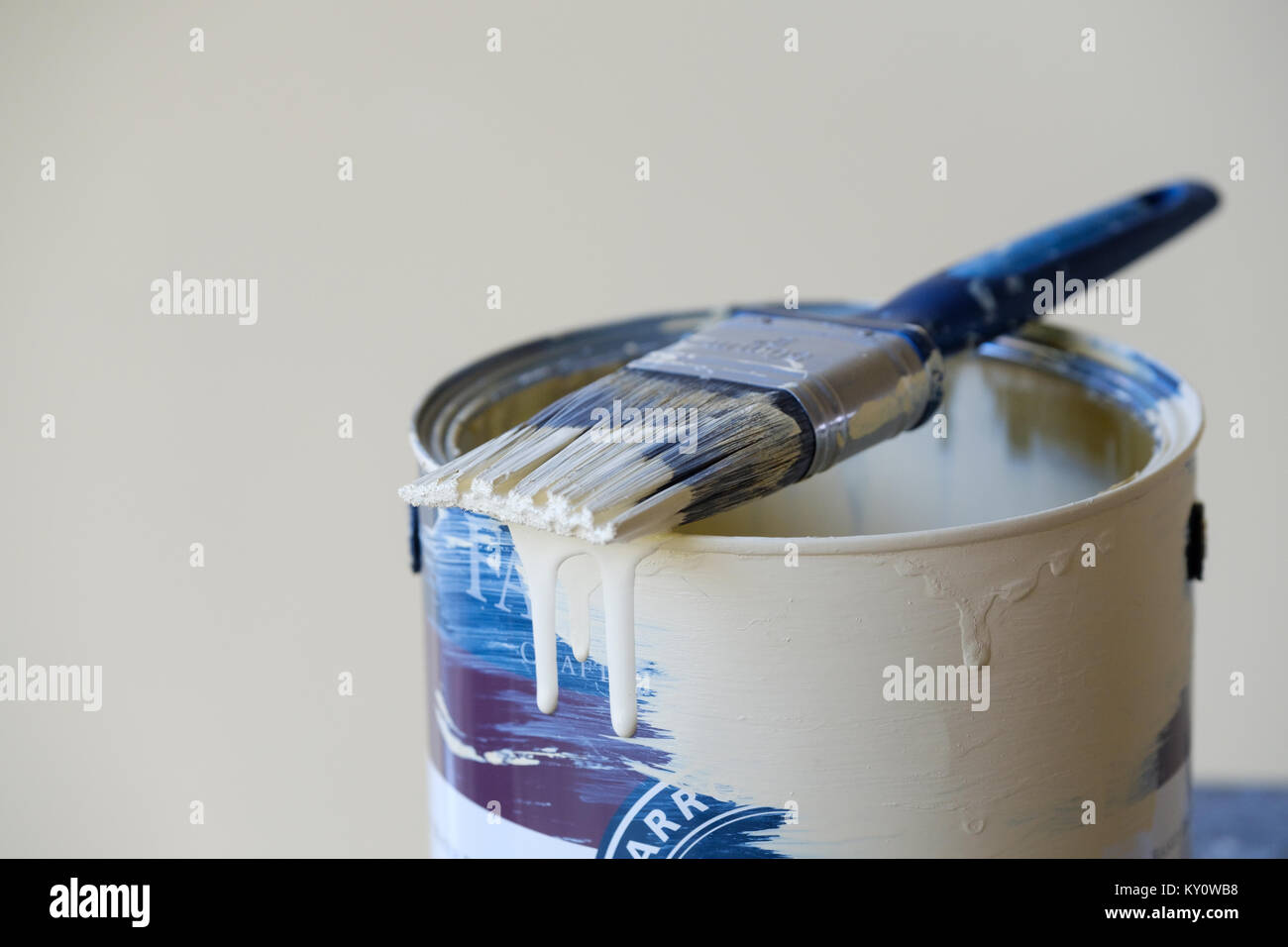 A half used tin of household interior wall paint with a used paint brush lying across the top of it. the brush is partially covered in wet paint Stock Photo