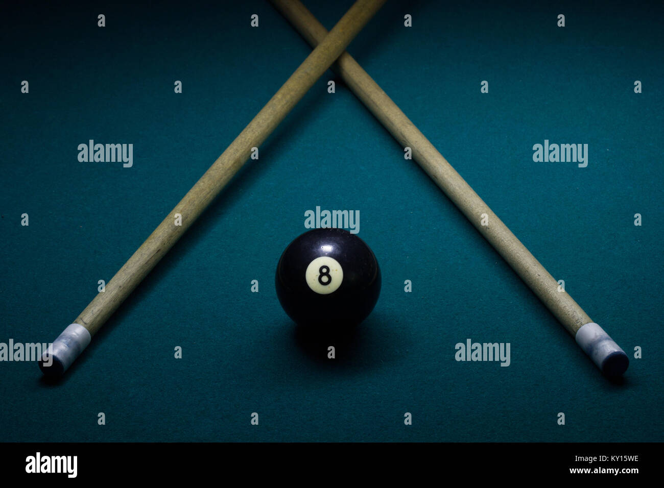 black eight ball on a green billiard table with two cue sticks in v shape Stock Photo