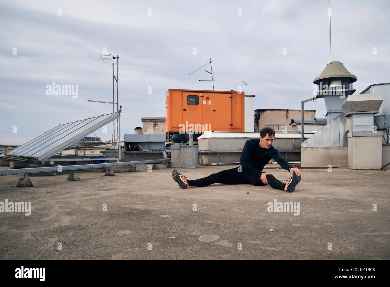 one young man stretching outdoors on rooftop of building. Heating, ventilation, and air conditioning systems. Stock Photo