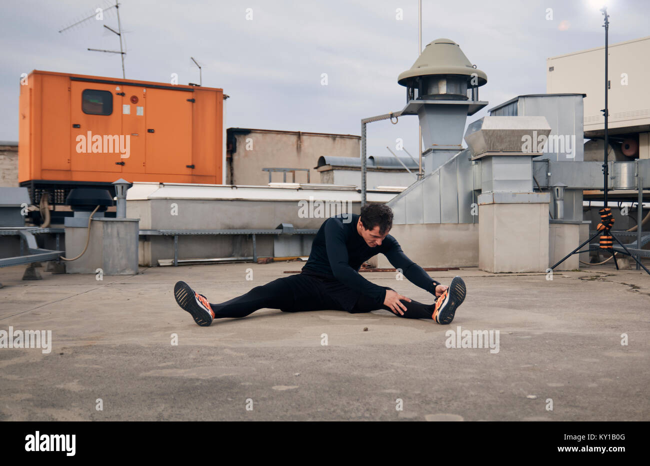 one young man stretching outdoors on rooftop of building. Heating, ventilation, and air conditioning systems. Stock Photo