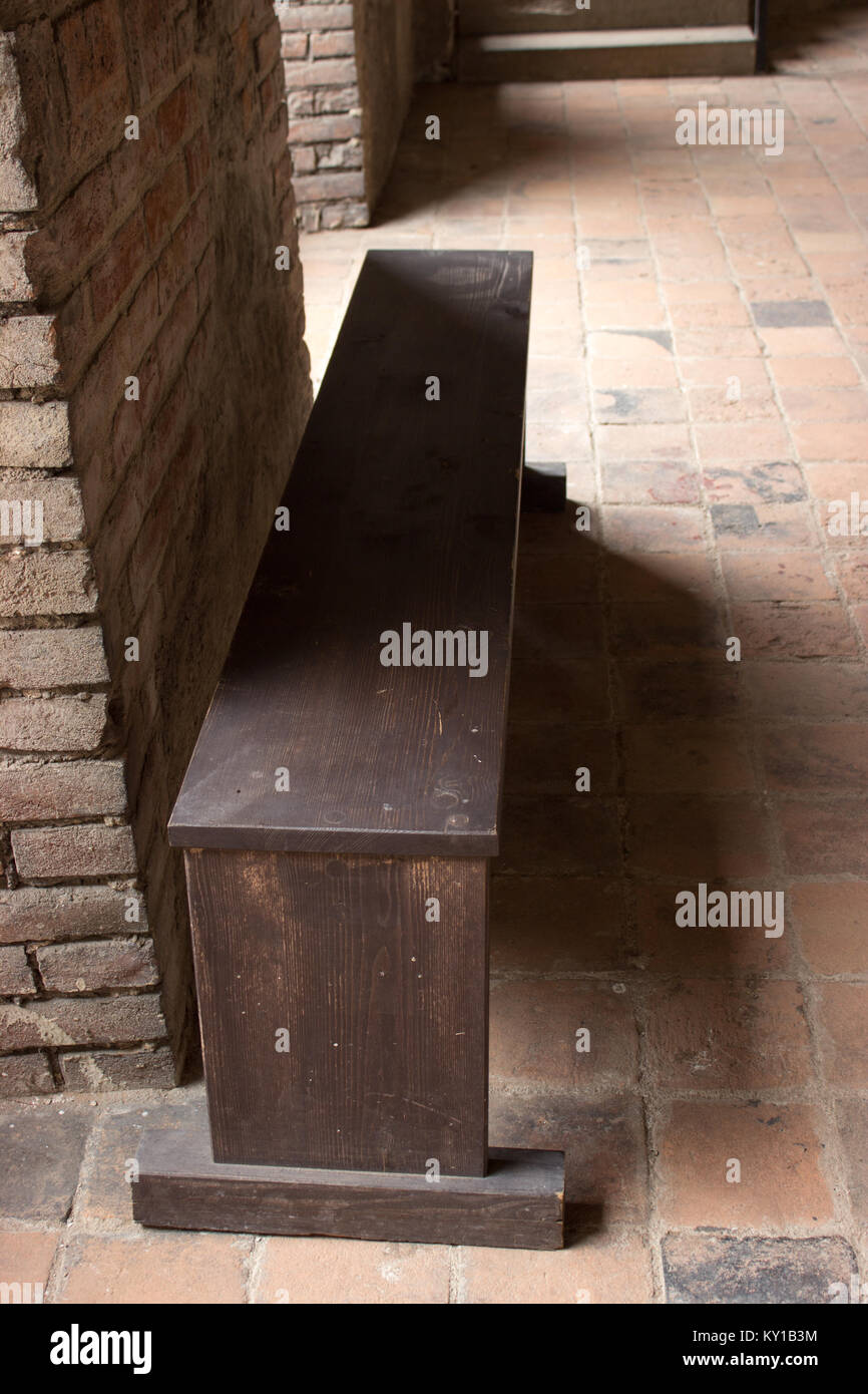 Wooden bench stands at a brick wall in the old castle corridor. Stock Photo