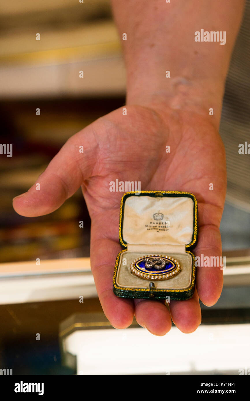 The Art Antiques & Interiors Fair, London, UK. Greg Turnbull holds a Victorian gold brooch with a diamond Staffordshire knot on blue enamel surrounded Stock Photo