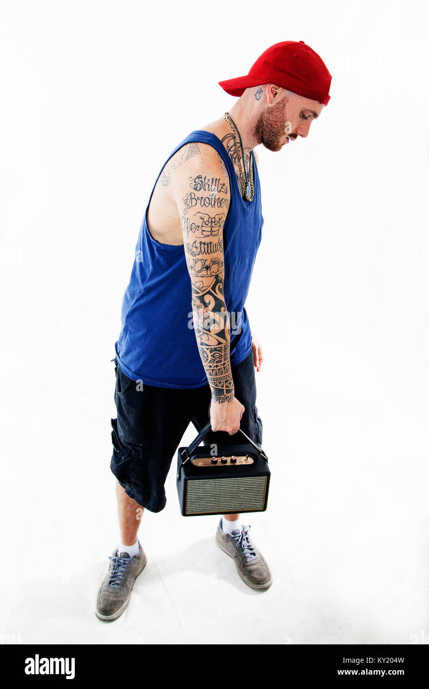 standing tattooed rap singer posing in studio with an amplified radio on a white background Stock Photo