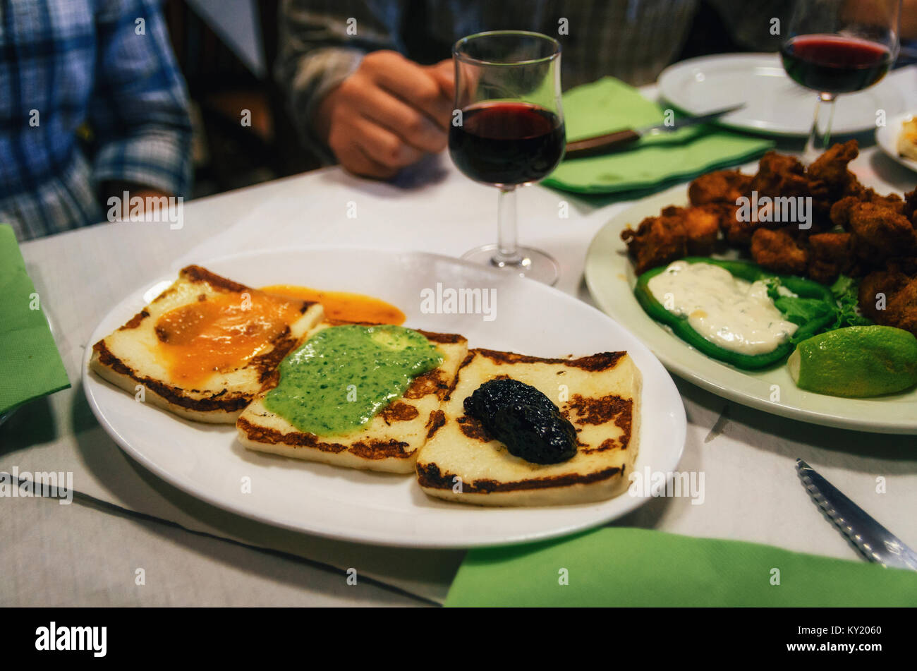 Traditional tapas plate with grilled cheese with canarian sauces mojo rojo, mojo verde and alioli, and glasses of red wine on background, Tenerife, Ca Stock Photo