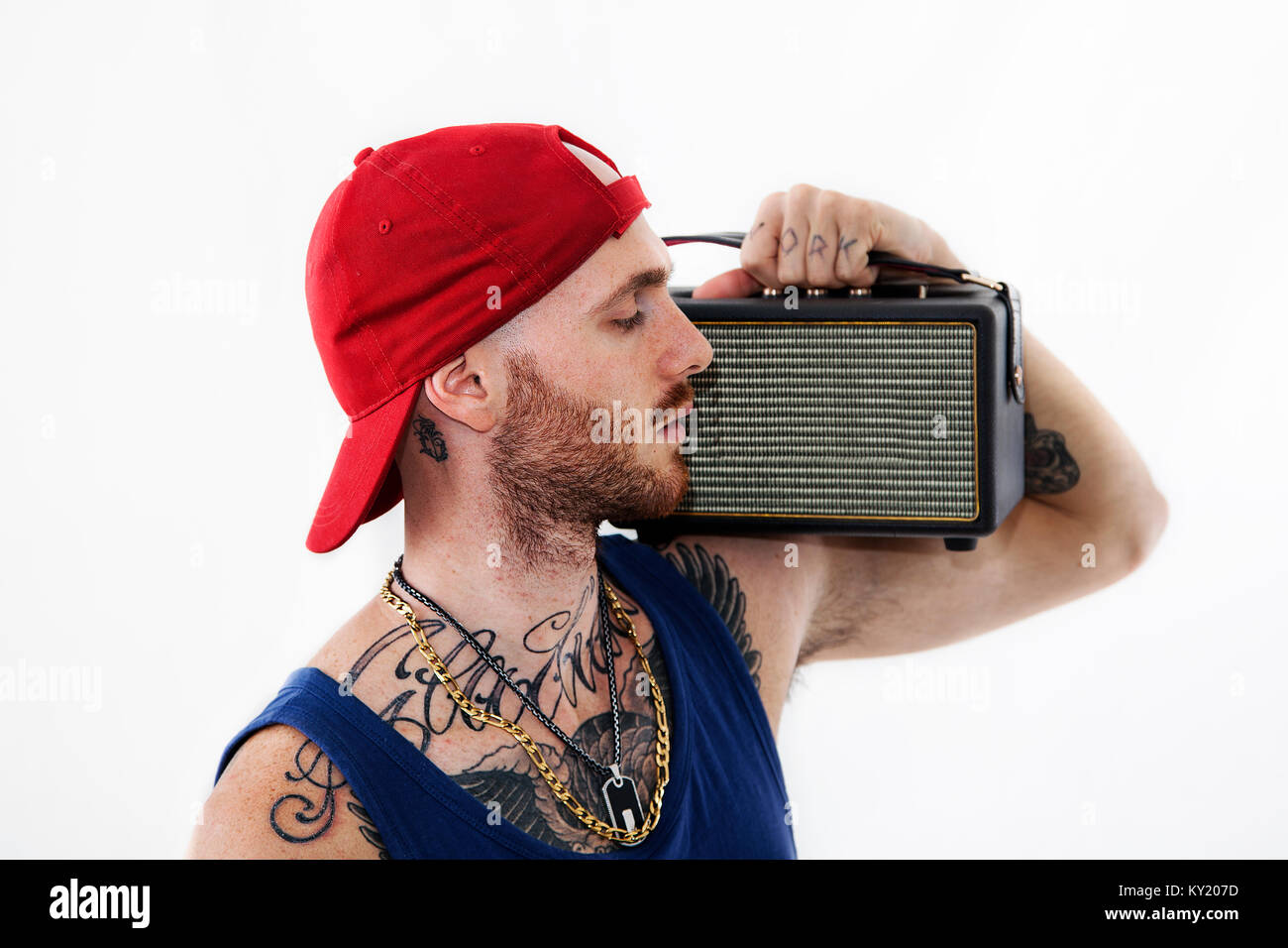 standing tattooed rap singer posing in studio with an amplified radio on a white background Stock Photo
